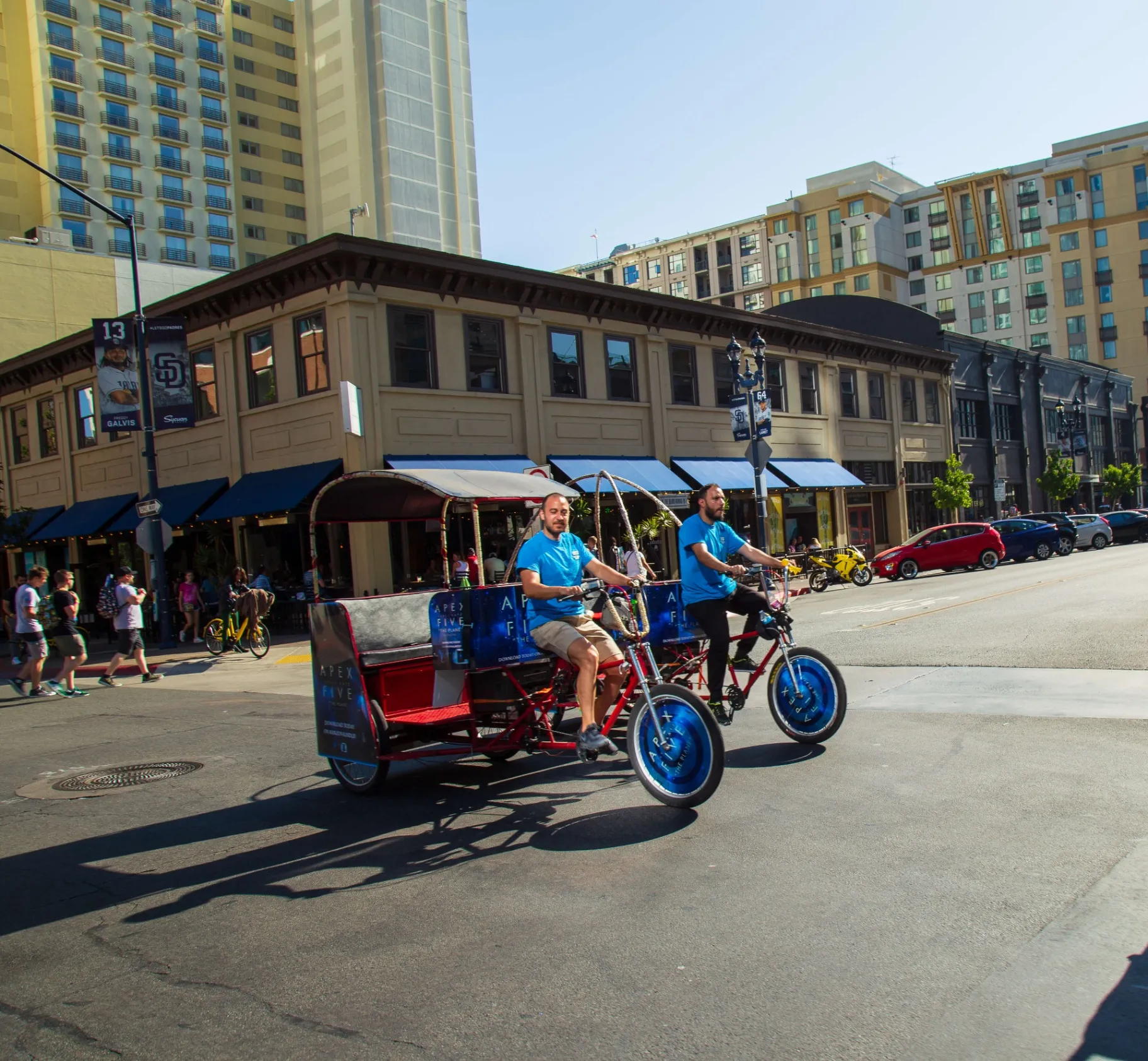Two Apex Five branded pedicabs crossing downtown San Diego street