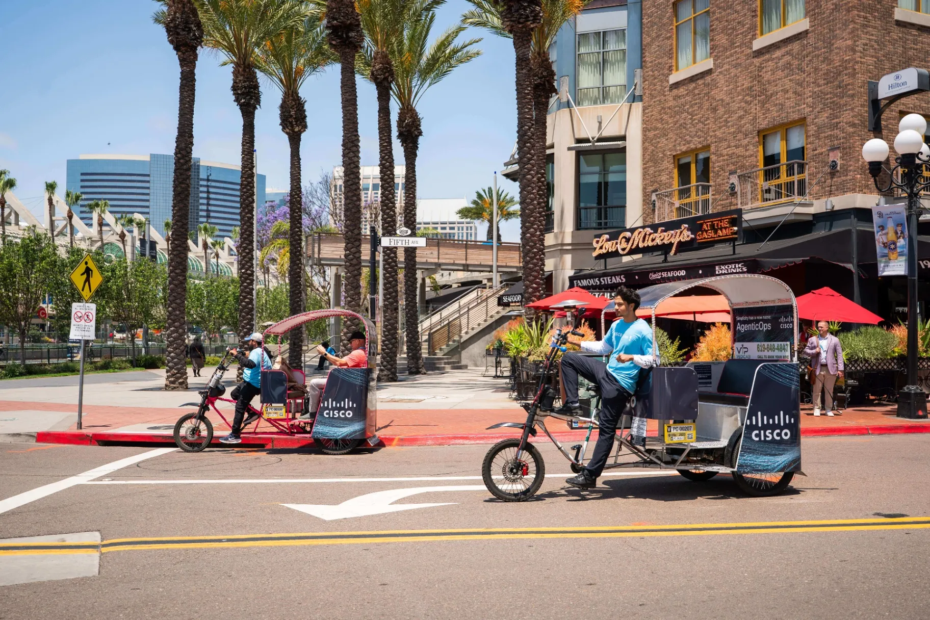 Two Cisco branded electric pedicabs cruising through Downtown San Diego streets