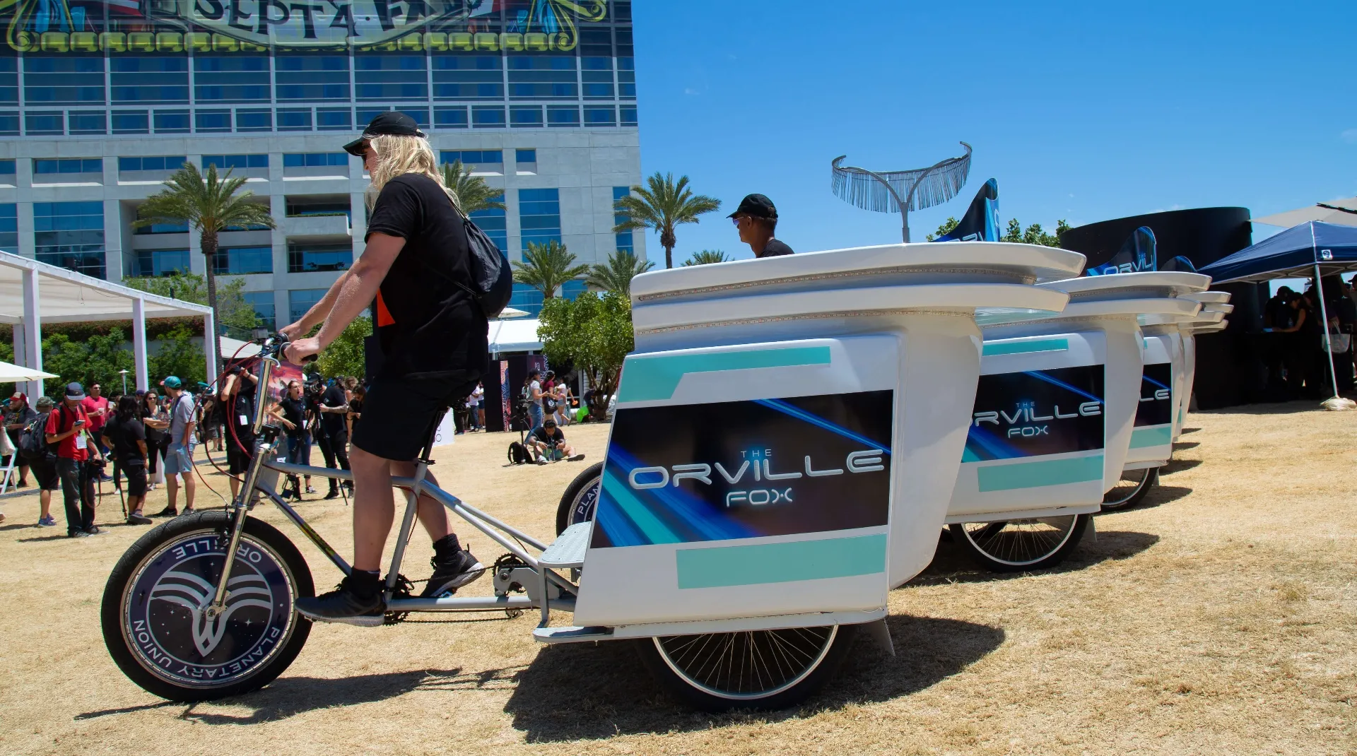 Orville pedicab rider passing campaign crowd at COSMOS event